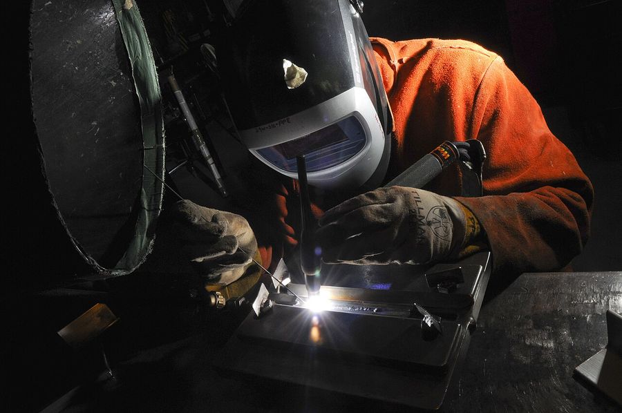 Welder in a protective helmet TIG welding a metal part